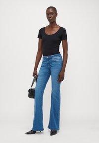 Svart kortärmad bodysuit, blå utsvängda jeans, slät denimtextur, medelhög midja, framhävd sömnad, tillsammans med en liten svart handväska.