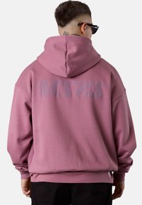 Oversized pink hoodie with a drawstring hood, ribbed cuffs, and a smooth texture. Features large, subtle logo on the back.