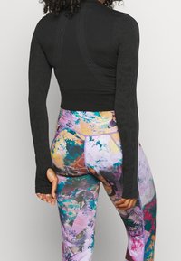 Svart långärmad träningsoverdel med texturerad design och figurnära passform, kombinerad med färgglada, mönstrade högmidjade leggings med abstrakta former.