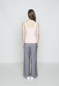 Light pink fitted tank top paired with wide-leg gray pinstriped trousers. White athletic shoes visible at the bottom. Plain background.