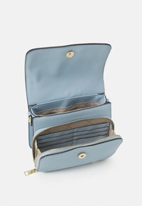 Vaaleansininen lompakko, jossa vetoketjusuljenta, kullanväriset metalliosat, useita korttipaikkoja ja sileä, teksturoitu pinta. Avoinna sisäosien näyttämiseksi.