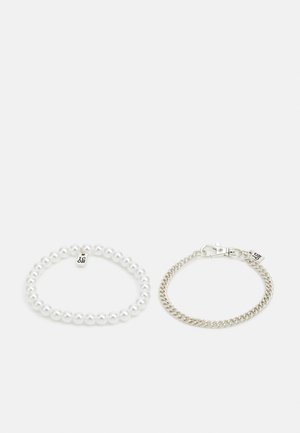 Deux bracelets : l'un est composé de perles blanches avec une petite étiquette, l'autre est une chaîne en argent avec un fermoir en forme de homard et une étiquette.