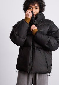 Schwarze Daunenjacke mit hohem Kragen, Reißverschluss und gerippten Bündchen. Verfügt über eine matte Oberfläche und einen verstellbaren Saum für eine bequeme Passform.