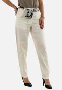 Pantalon blanc à coupe décontractée, avec une ceinture en tissu à motif nouée à la taille et associé à des escarpins noirs.