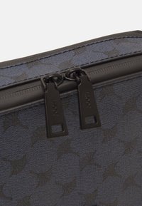 Schwarze und blaue Tasche mit gemustertem Design aus strukturiertem Stoff, ausgestattet mit einem doppelt zippbaren Verschluss aus schwarzem Metall und kontrastierenden Nähten.