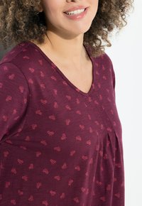 Top bordeaux con scollatura a V e maniche corte, caratterizzato da un sottile motivo di piccole forme rosa, realizzato in un tessuto morbido e strutturato.