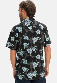 Cămașă neagră cu mânecă scurtă, cu un model floral, având flori de un albastru deschis și frunze verzi, fabricată din material ușor, cu o croială lejeră.