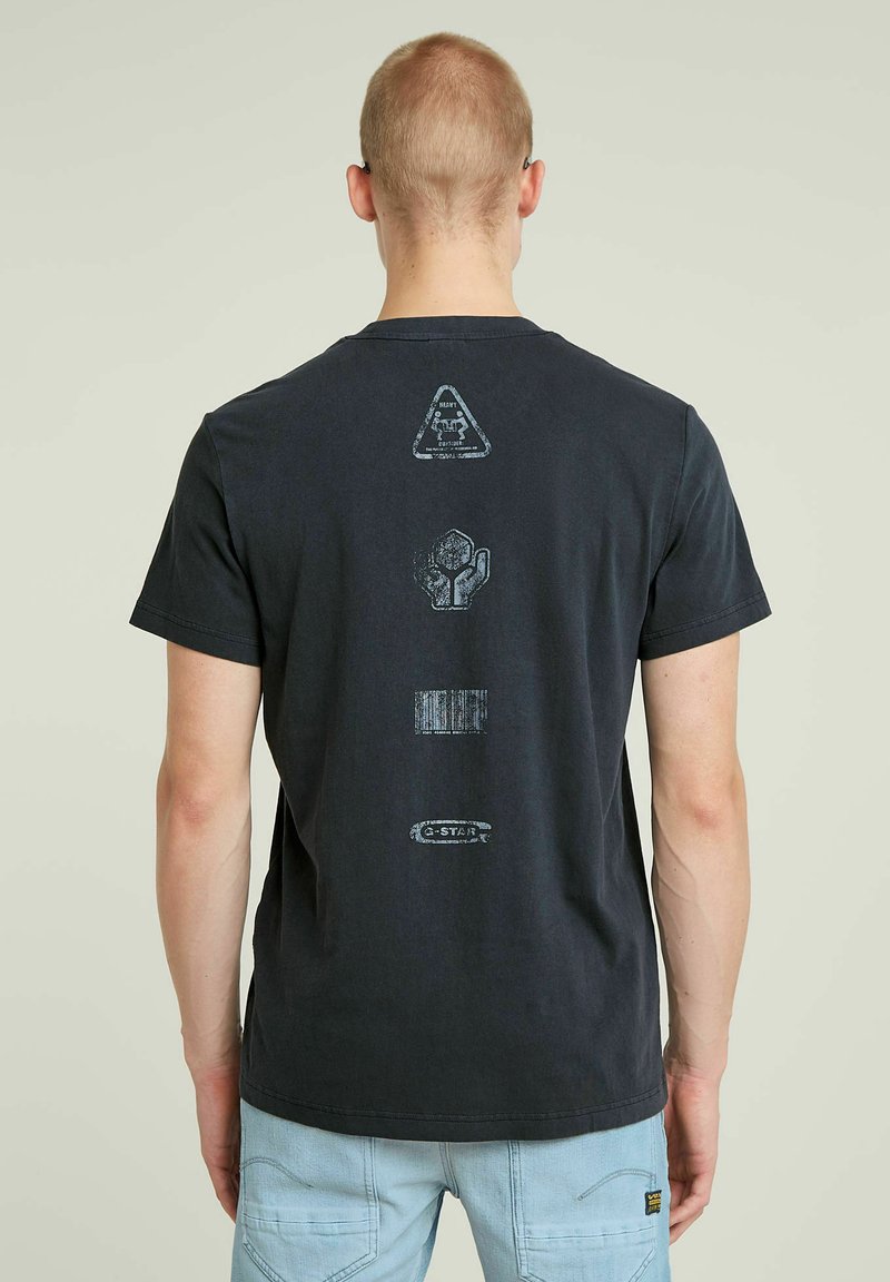 Sort bomulds t-shirt med grafiske tryk på ryggen: advarselssymbol, kaktus, stregkode og "G-STAR" logo, rund hals, korte ærmer.