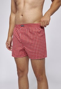 Rote karierten Boxershorts aus einem weichen Stoff, mit einem schwarzen elasticen Bund, der mit "SNOCKS" beschriftet ist, und einem Knopfdetail an der Vorderseite.