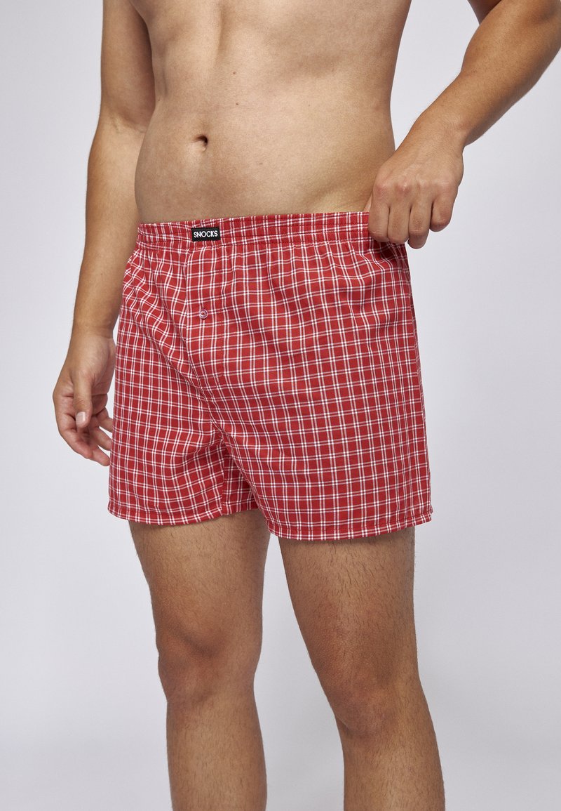 Rote karierten Boxershorts aus einem weichen Stoff, mit einem schwarzen elasticen Bund, der mit "SNOCKS" beschriftet ist, und einem Knopfdetail an der Vorderseite.