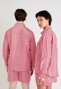 Rot-weißer Karomuster-Anzug mit passendem Hemd und Shorts. Aus Baumwollmaterial, mit lockerer Passform und langen Ärmeln, die Knopfdetails aufweisen.