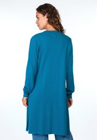 Türkisfarbener langer Cardigan aus strukturiertem Stoff, mit einer lockeren Passform und gerippten Bündchen. Seitliche Schlitze verbessern die Beweglichkeit und den Komfort.