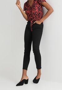 Top envolvente de estampado de leopardo rojo y negro con mangas cortas, combinado con pantalones negros ajustados y zapatillas negras con punta afilada y tacón bloque.