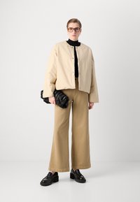 Beige cropped jacket with a round neckline, paired with black turtleneck, tan wide-leg pants, and chunky black loafers. Black clutch bag.