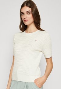 Πλεκτό λευκό πουλόβερ με υφή, κοντά μανίκια, ριμπς λαιμόκοψη και τελείωμα, με κόκκινες και μπλε λεπτομέρειες στους καρπούς.