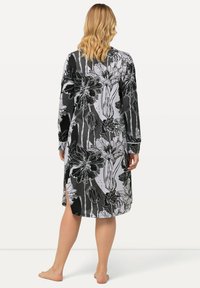 Abito floreale in bianco e nero con maniche lunghe, taglio a mezza lunghezza e spacchi laterali. Il tessuto ha una texture liscia.