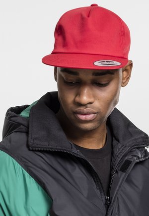 Rød snapback-kasket med flad skygge, lavet af struktureret stof. Bæres med en sort og grøn puffy jakke.