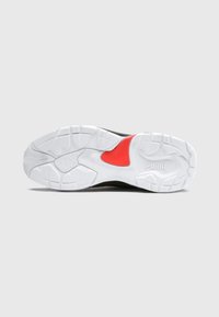 Biała podeszwa sportowego buta z teksturowanymi wzorami i czerwonym akcentem; zawiera logo marki oraz przeważającą czarną sekcję.