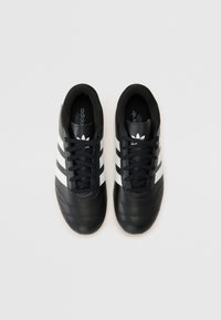 Chaussures de soccer en cuir noir avec trois bandes blanches, design à lacets, col rembourré et surface texturée pour une adhérence optimale.