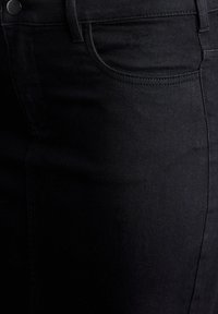 Černá džínová sukně s hladkou texturou, vybavená přední kapsou a jemnými detaily šití. Materiál je elastický a těsně obepíná postavu.