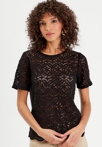 Top in pizzo nero con maniche corte, motivo floreale, scollo rotondo e bordi ondulati. Tessuto semitrasparente e vestibilità rilassata.