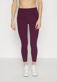 Löydä korkeavyötäröiset violetit legginsit, jotka on valmistettu joustavasta materiaalista ja joissa on sileä pinta sekä litteät saumat, yhdistettynä valkoisiin urheilujalkineisiin.
