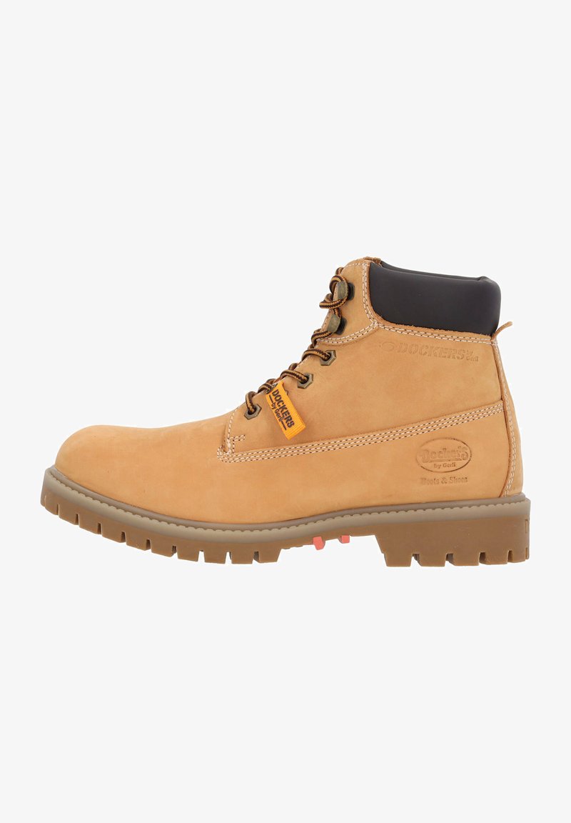 Tan suède werklaars met een zwarte gevoerde kraag, bruine rubberen zool, metalen ogen en een oranje merklabel. Beschikt over een verstevigde neus en een gestructureerde afwerking.