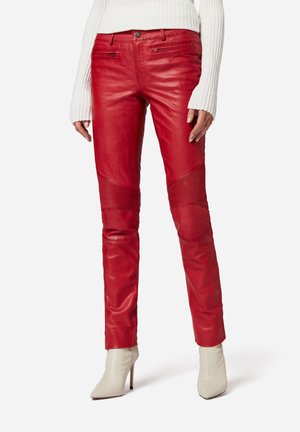 Pantalons en cuir rouge avec une coupe ajustée, présentant des panneaux texturés et des poches zippées. Associés à des bottines blanches à talons hauts.