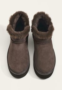 Barna velúr bokacsizma puha szőrmével bélelt szegéllyel, kerek orral és lapsz sole-lal. Látható fémrész vagy minta nélkül.