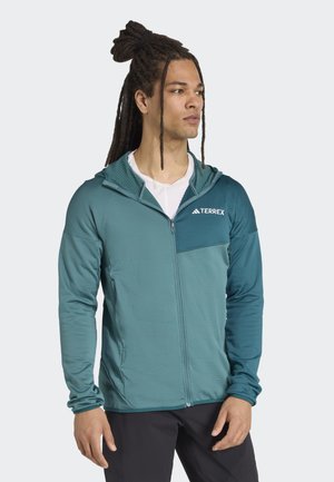 Haut à zip couleur bleue-vert avec une capuche texturée et une poche poitrine. Dispose de manches longues et d'un tissu léger et respirant.
