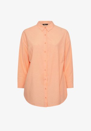 Chemise à manches longues couleur pêche clair, avec des boutons, un col pointu et un ourlet arrondi, présentée sur un fond blanc.