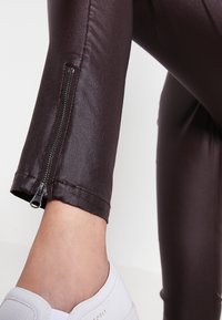 Blanka, mörkbruna leggings med en figurnära design, som har dragkedja vid ankeln och en slät yta. Åtföljda av vita sneakers.