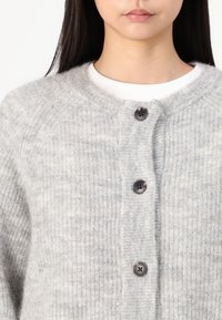 Cardigan en tricot gris fabriqué en matériau doux, doté d'un col rond, de cinq boutons et d'une texture côtelée avec un motif subtil.
