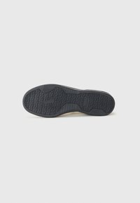 Suela de zapato de goma negra con un patrón de agarre texturizado, que presenta líneas en zigzag y formas geométricas elevadas para tracción y estabilidad.