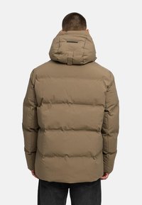 Brun puffjakke med høy krage, quiltet design og hette. Har en jevn tekstur og bakre aksentstripe nær nakken.