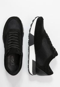 Baskets noires en mesh et daim avec une tige texturée, une fermeture à lacets et une semelle épaisse avec une bande accentuée blanche.