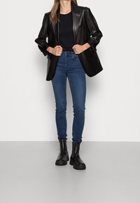 Blazer de cuero negro, top ajustado negro, jeans ajustados azules y botines negros. Texturas suaves y diseño entallado con silueta elegante.