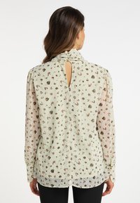 Bluză verde deschis cu imprimeu floral, mâneci lungi, decolteu plissetat, detaliu cu găură la spate și o textură netedă, transparentă.