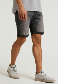 Pantaloni shorts neri in denim con finitura distressed, orli arrotolati e vestibilità slim, abbinati a sneakers grigio chiaro con un design testurizzato.