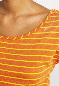 Oranssi T-paita, jossa on keltaisia vaakaraitoja, leveällä pyöreällä kaula-aukolla ja hienolla ompelulla. Hienovarainen brodeeraus olkapäällä.