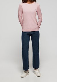 Vaaleanpunainen neulepusero, jossa on pyöreä kaula-aukko ja ribbauskaitaleet, yhdistetty tummansinisiin suoriin farkkuihin ja valkoisiin tennareihin.