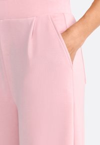 I pantaloni su misura rosa chiaro presentano tasche laterali, una trama liscia e un design pulito con sottili pieghe in vita.