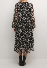 Robe à manches longues à motifs noirs et blancs, avec une taille cintrée, un tissu transparent et une silhouette fluide. Accentuée d'un col montant.