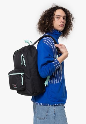 Mochila negra hecha de un tejido duradero con cremalleras y acentos de color azul claro. Cuenta con un bolsillo frontal y correas ajustables. Se lleva en el hombro.