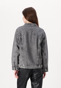 Gray denim jacket with a relaxed fit, button closures at the waist, and visible stitching. Features a classic collar and a textured finish.