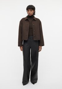 Bruine wolmix cropped jas met grote knopen, gecombineerd met high-waisted zwarte leren broeken met een gladde afwerking en een lichte flare.