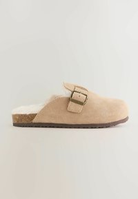 Sabot en suède beige avec une doublure douce et duveteuse, sangle ajustable avec une boucle en bronze et une semelle en caoutchouc texturé marron.