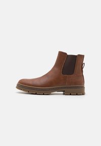 Bottine en cuir marron avec panneaux latéraux élastiques, surface texturée, languette de tirage et semelle robuste. Présente un bout rond et des coutures contrastées.