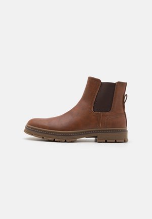 Bota de cuero marrón hasta el tobillo con paneles laterales elásticos, superficie texturizada, lengüeta para tirar y suela resistente. Presenta una puntera redonda y costuras en contraste.