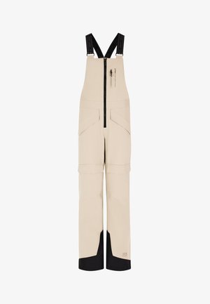 Pantalons bretelles imperméables beiges avec sangles noires ajustables, une fermeture éclair à l'avant et plusieurs poches ; présente des accents noirs au niveau de l'ourlet.